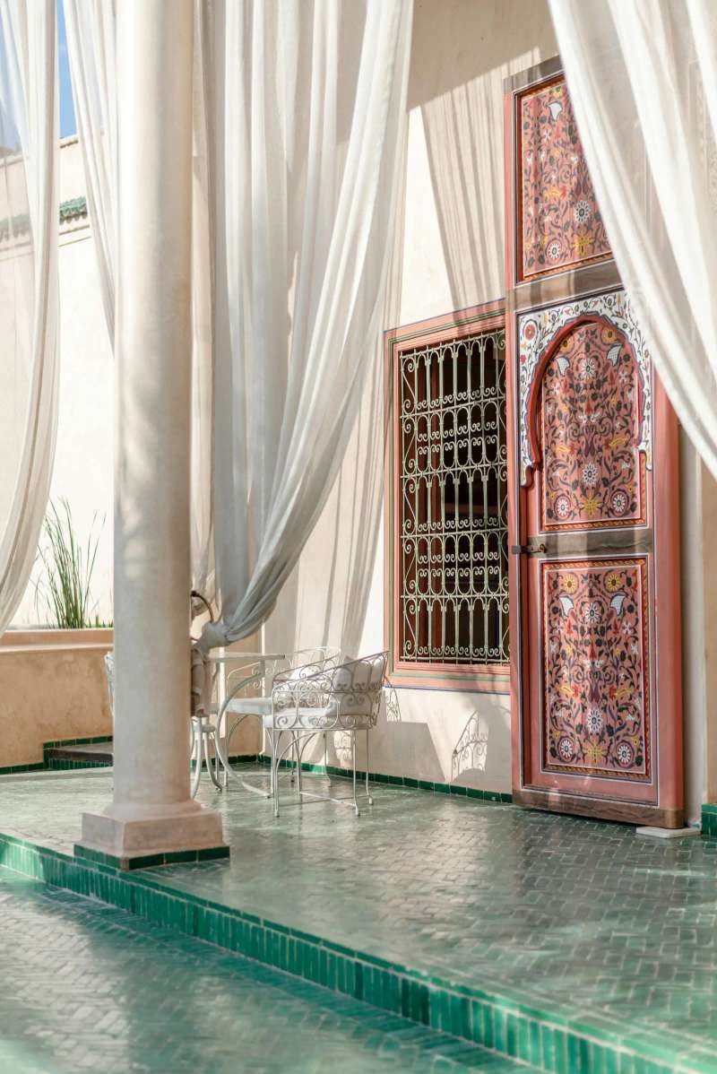 Traditional riad terrace with green zellige tiles and flowing curtains overlooking Moroccan medina rooftops