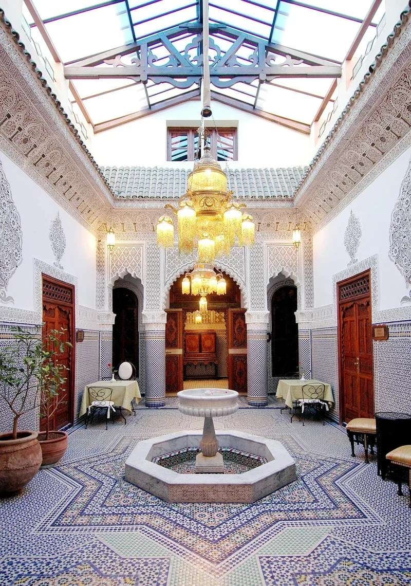 Traditional Moroccan riad interior courtyard with central fountain surrounded by ornate zellige tilework and arched doorways