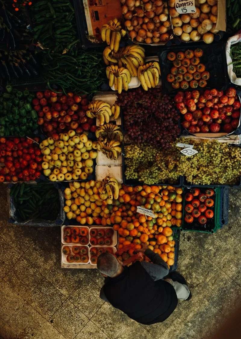 Overhead view of vibrant Moroccan fruit market stall displaying fresh bananas, grapes, apples, tomatoes, and seasonal produce in colorful abundance representing Morocco's agricultural richness